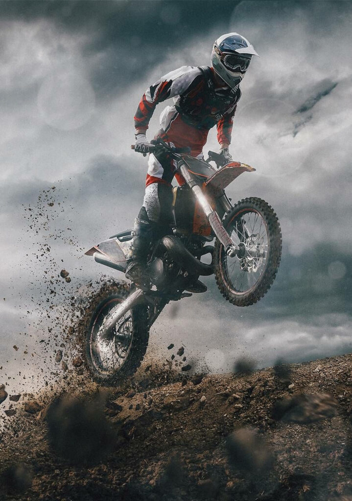 Dirt bike rider mid-air over rugged terrain with dramatic cloudy sky intense motocross action Wallpaper