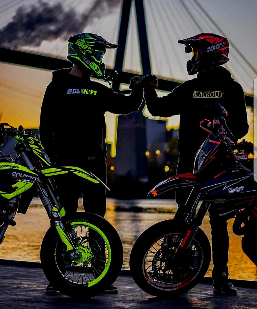 Motocross Riders Fist Bump at Sunset - Vibrant Wallpaper Background