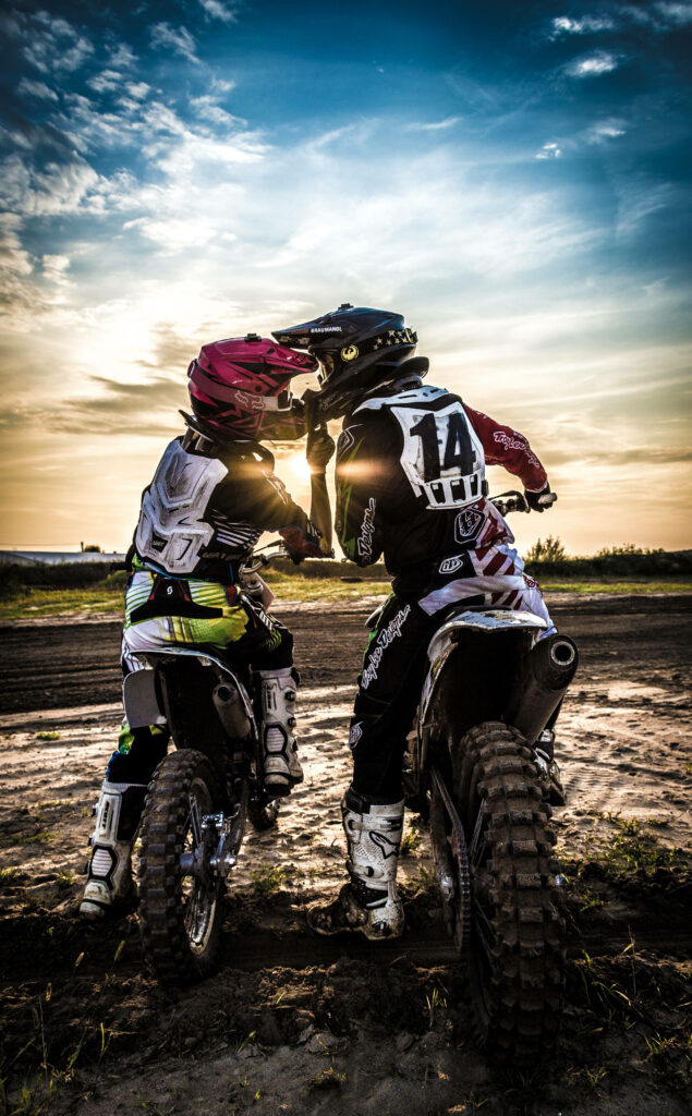 Candid Motocross Riders: Scenic Evening Sky Wallpaper Background
