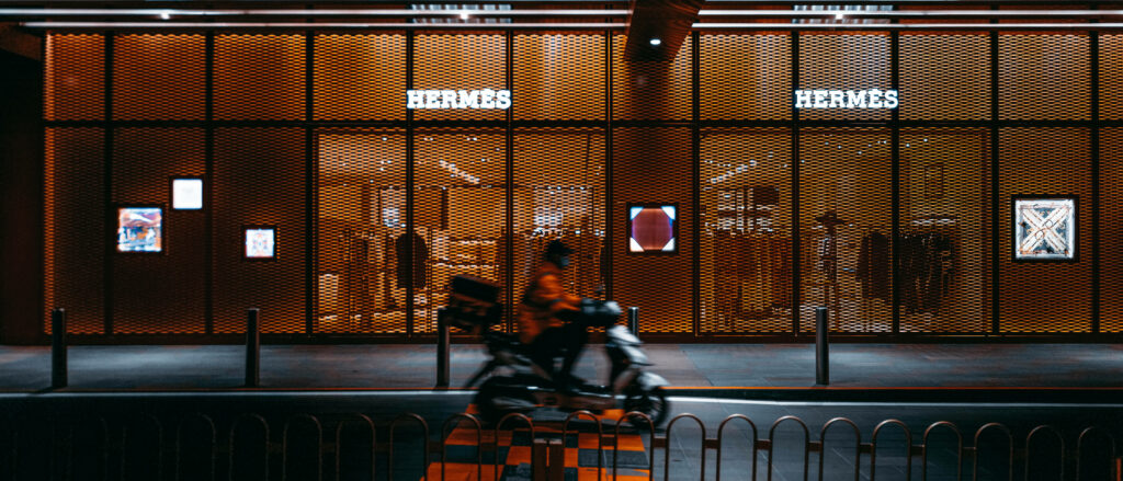 Motorcycle riding past illuminated Hermès store at night vibrant urban street wallpaper background