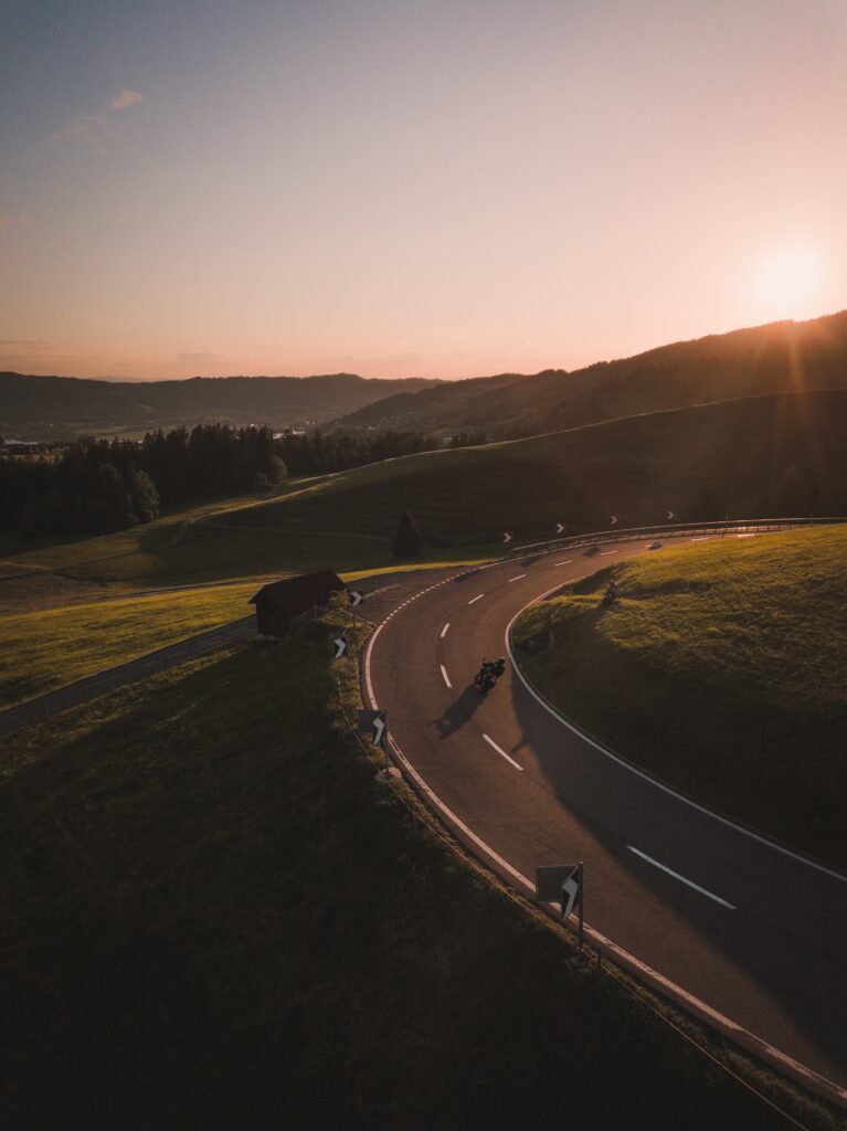 Motorcyclist riding winding road through green hills at sunset scenic wallpaper background