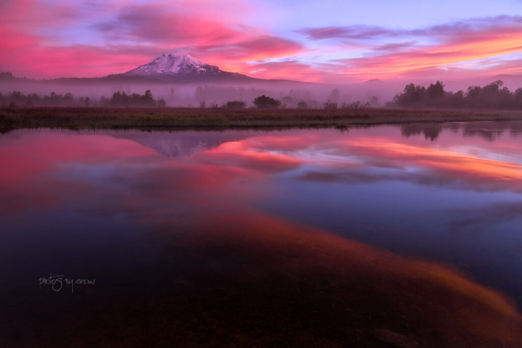 Mount Adams volcano at sunrise with vibrant pink purple orange sky reflected on calm lake Wallpaper