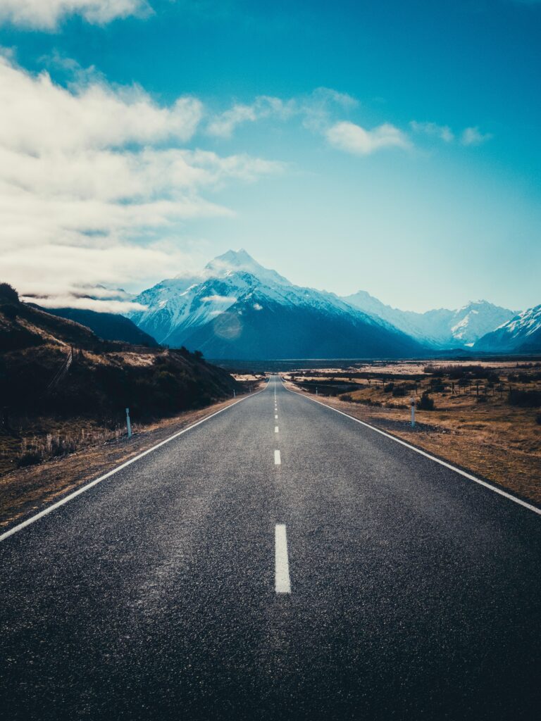 Asphalt road to Mount Cook New Zealand with snowy peak golden fields rugged mountains blue sky Wallpaper
