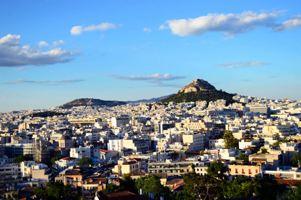 Panoramic view of Mount Lycabettus above Athens cityscape under partly cloudy blue sky wallpaper