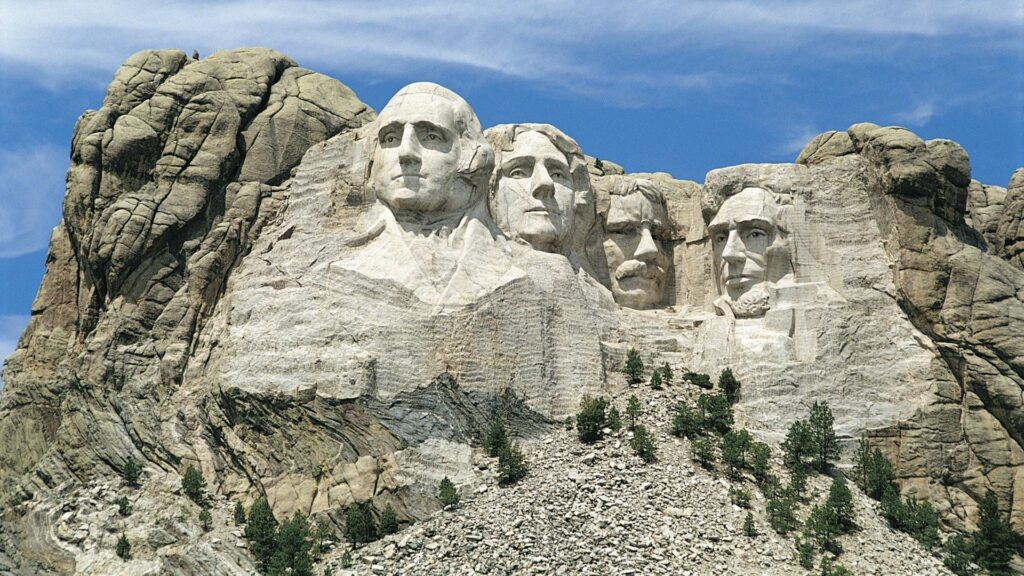 Mount Rushmore carved faces sculpture with natural rock textures under blue sky wallpaper