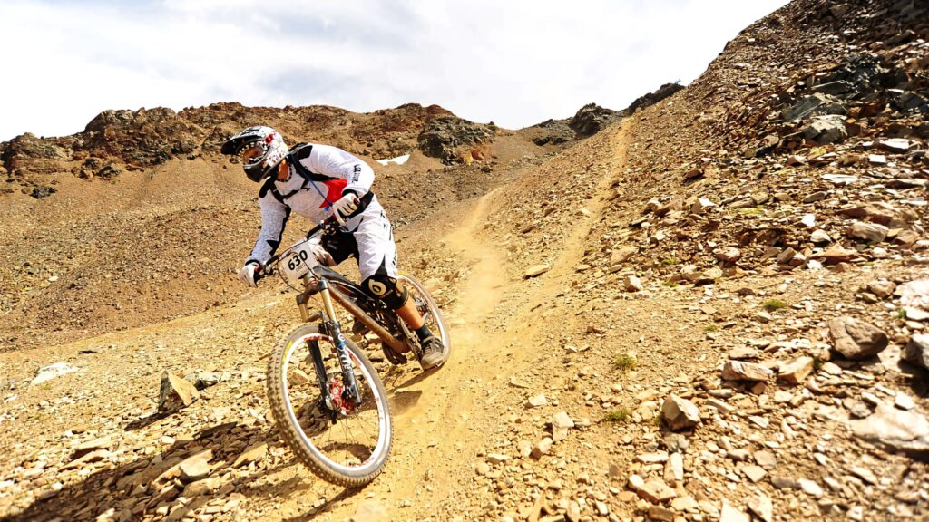 Mountain biker in full gear rides rugged dirt trail through rocky terrain off-road cycling adventure Wallpaper