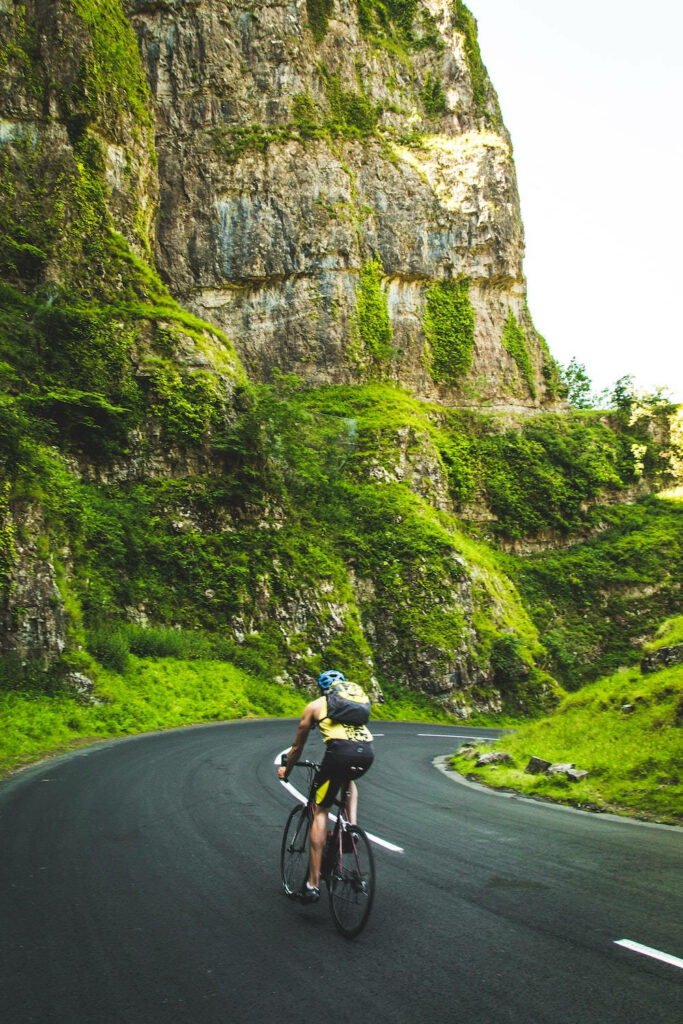Cyclist riding winding mountain road surrounded by lush greenery and rocky cliffs nature wallpaper