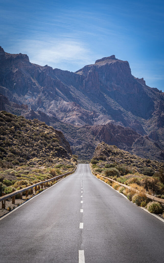 Straight road through rugged mountains with clear blue sky and natural vegetation wallpaper background