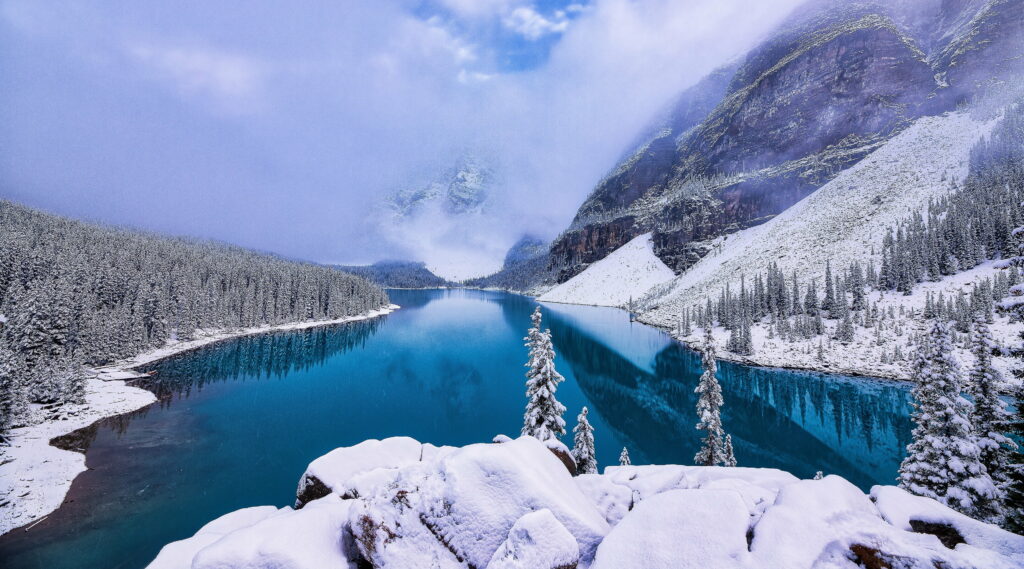 Moraine Lake winter landscape with turquoise waters snow-covered pines and misty mountains Wallpaper