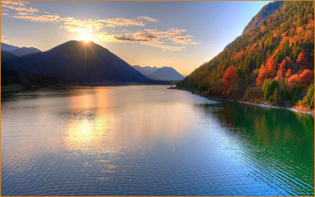 Autumn sunset over Sylvensteinsee lake Bavaria with vibrant fall foliage and mountain peak Wallpaper