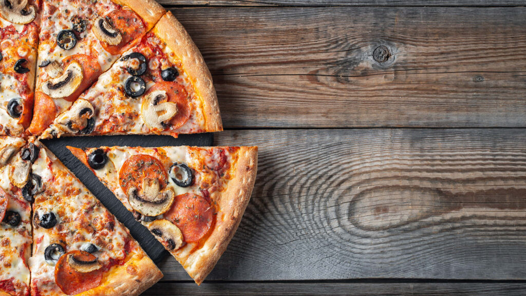 Delicious pepperoni mushroom black olive pizza slice on rustic wooden table closeup view Wallpaper