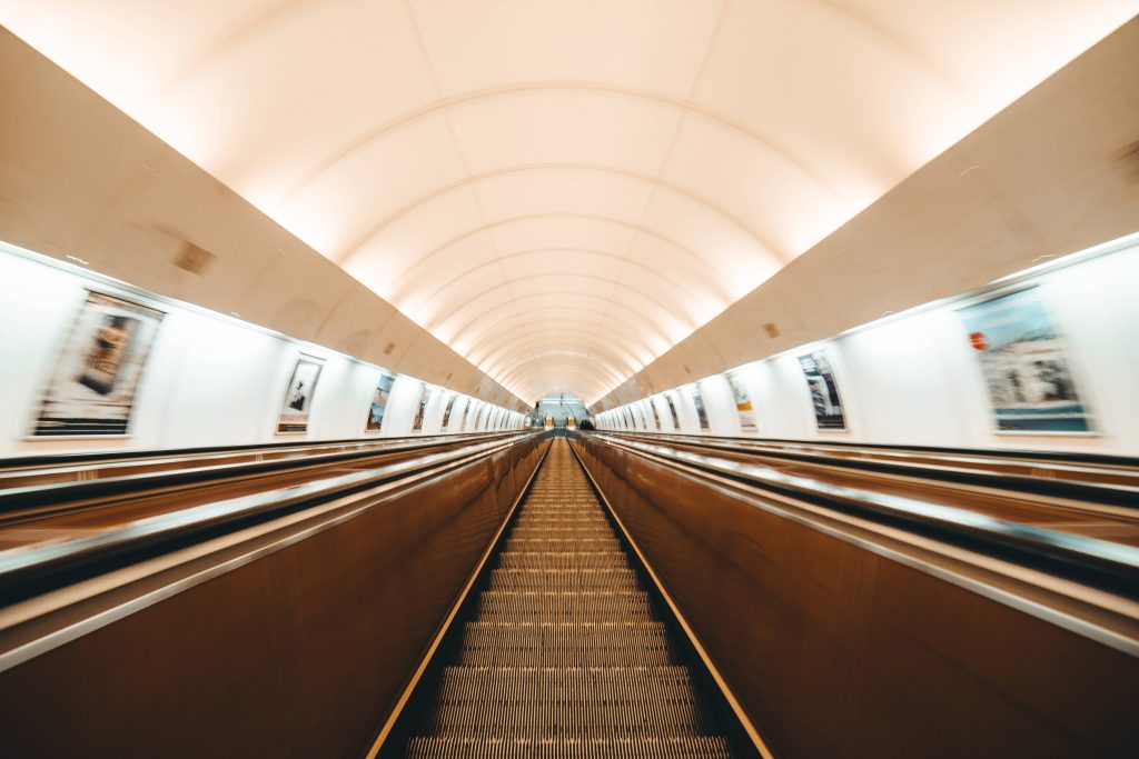Symmetrical underground metro escalator with warm vaulted lights and cool side walls wallpaper