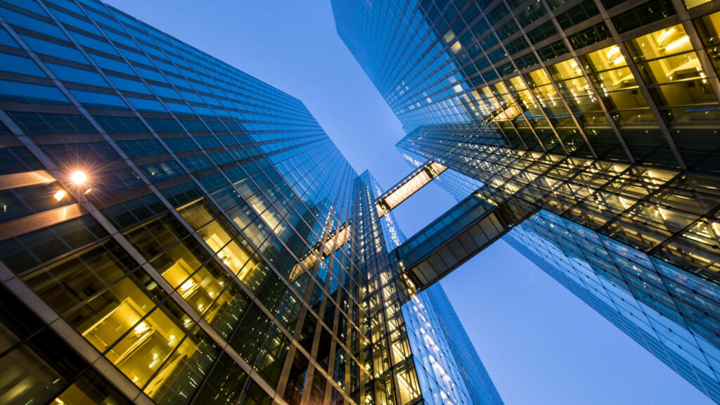 View looking up between glass high rise buildings in Munich with warm lights and evening sky Wallpaper