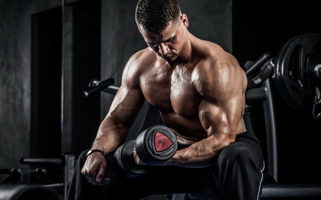 Muscle-Building Symphony: HD Wallpaper featuring a Dumbbell-Clad Bodybuilder in Intense Workout