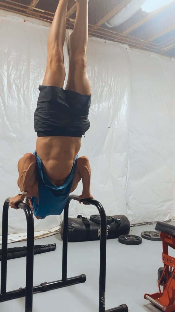 Muscular athlete handstand on black parallettes in home gym workout motivation wallpaper background