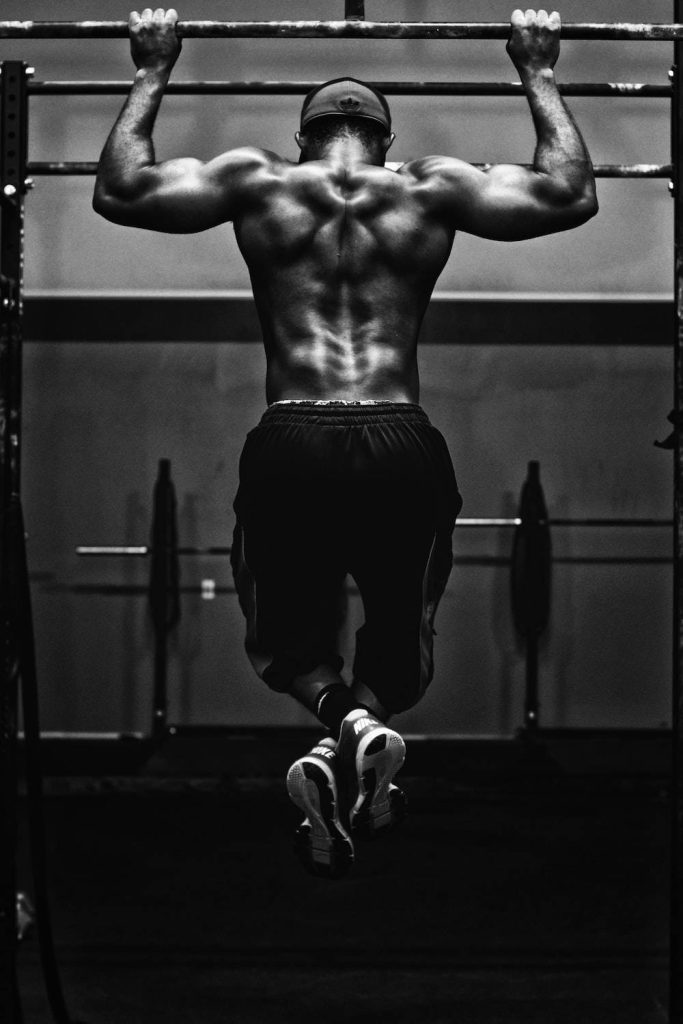 Black and white photo of muscular athlete doing pull ups highlighting strength and muscle definition Wallpaper