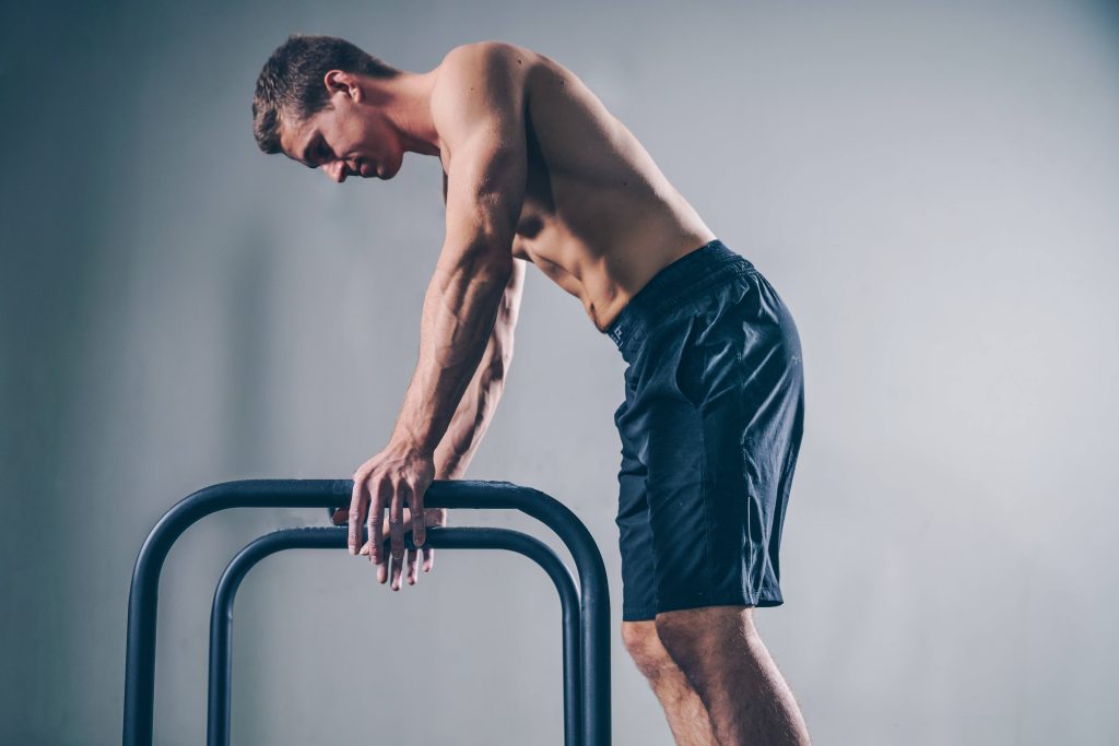 Muscular athlete gripping parallel bars in grey studio workout wallpaper for fitness motivation