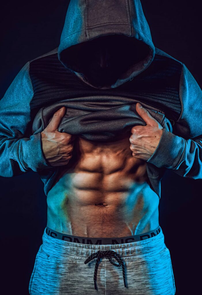 Muscular bodybuilder in hoodie reveals sculpted abs against dark background HD wallpaper