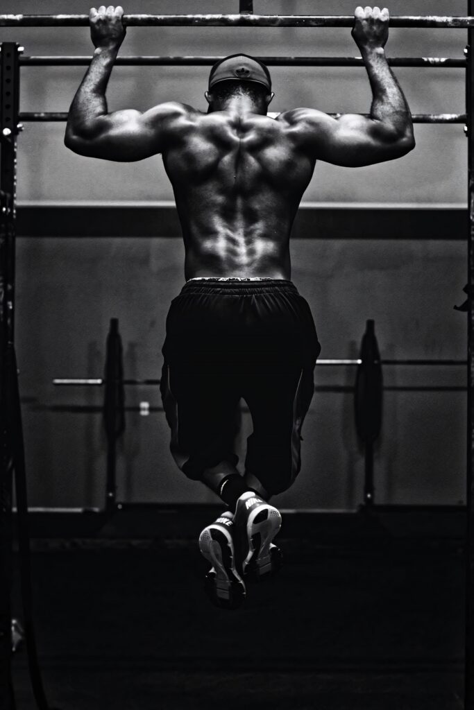 Muscular bodybuilder showcasing strength and muscle definition doing pull-up on monkey bar black and white wallpaper