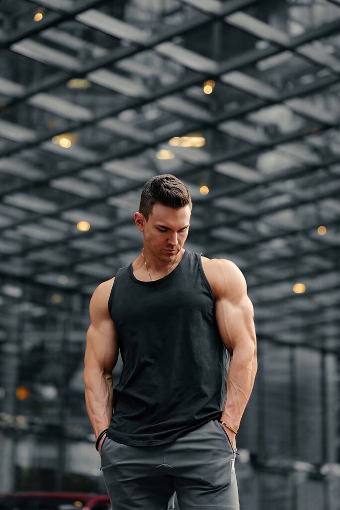 Muscular bodybuilder in black tank top posing confidently in urban setting with geometric ceiling Wallpaper