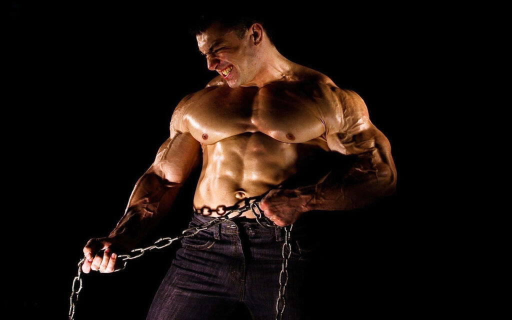 Muscular bodybuilder posing with metal chain on dark background showing intense strength Wallpaper