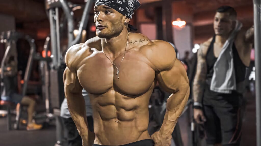 Muscular bodybuilder posing confidently in gym with defined physique and fitness equipment background Wallpaper