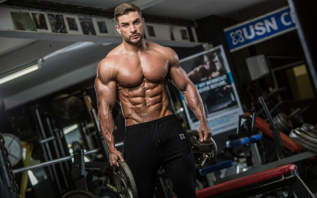 Muscular bodybuilder posing confidently in gym showcasing impressive physique and determination Wallpaper