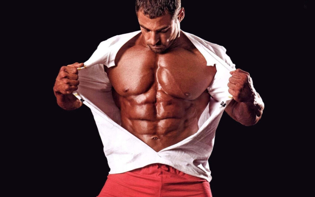 Muscular male bodybuilder tearing white shirt revealing defined abs and strong physique dark background Wallpaper