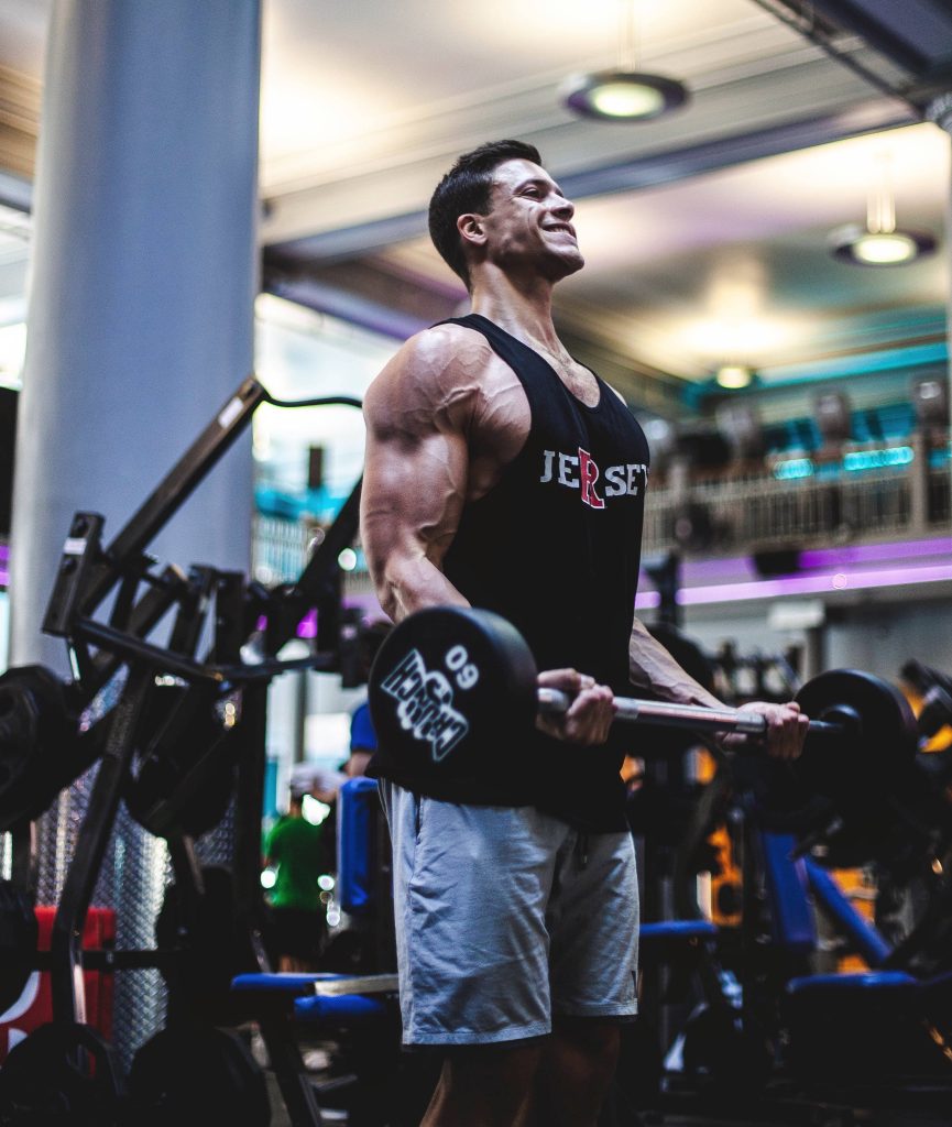 Muscular man doing intense barbell curls at Crunch gym showcasing vascularity and strength Wallpaper
