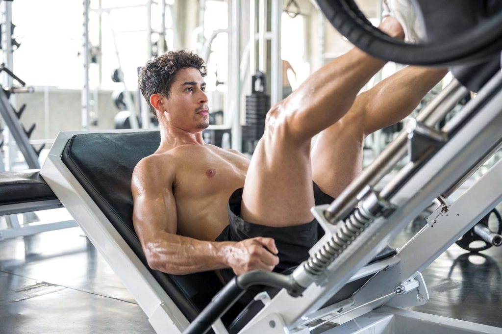 Muscular man doing unilateral leg press workout in bright modern gym with intense focus Wallpaper