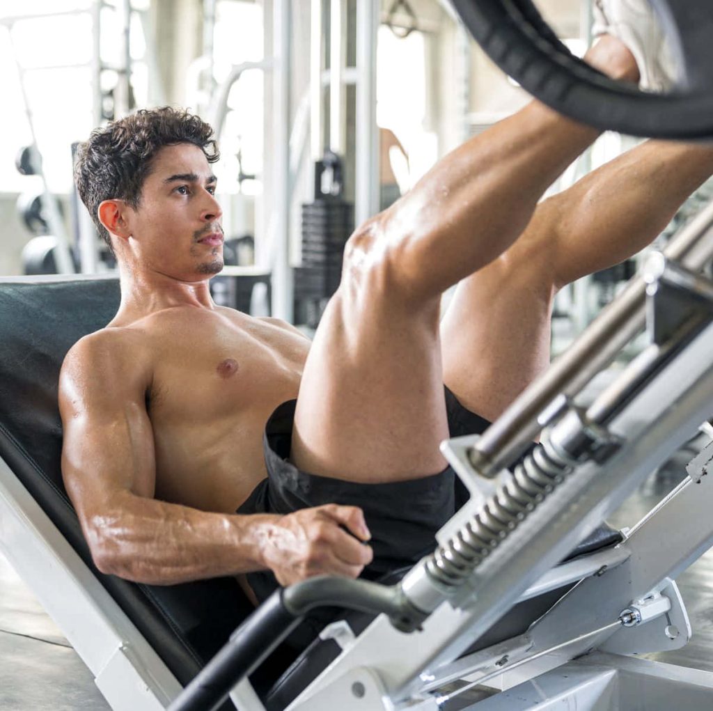 Muscular shirtless man focused performing leg press gym workout realistic lighting fitness wallpaper