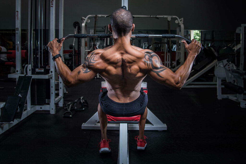 Muscular man with tattoos doing lat pulldown exercise showing defined back muscles in gym Wallpaper