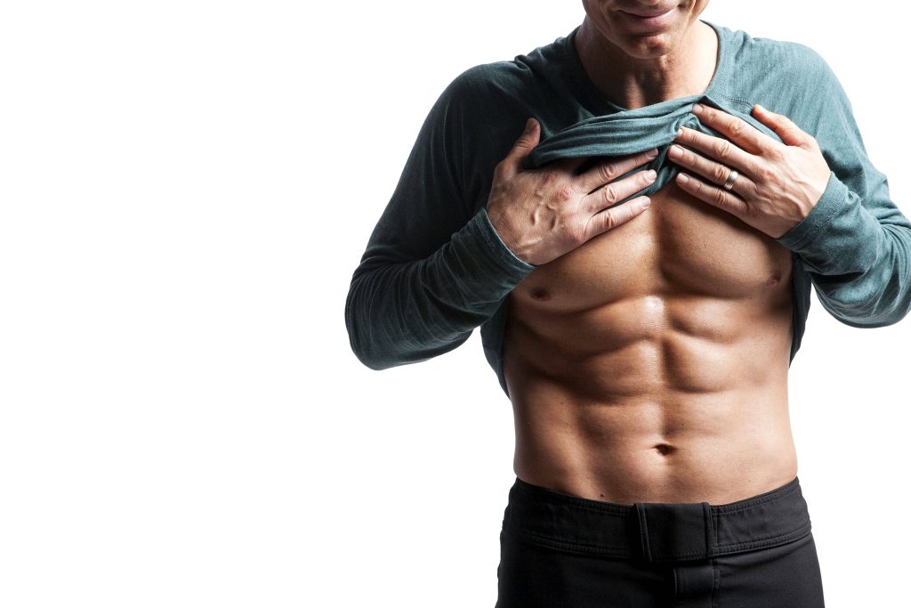 Muscular man lifting dark teal shirt showing toned abs with sharp studio lighting on white background Wallpaper