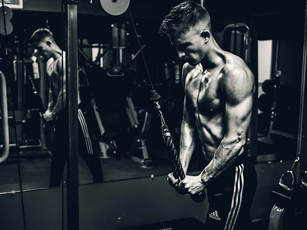 Muscular man doing tricep rope cable pushdowns in gym with mirrored wall intense workout Wallpaper