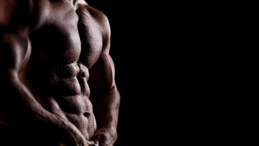 Muscular man with defined abs and strong arms posing against dark wallpaper background