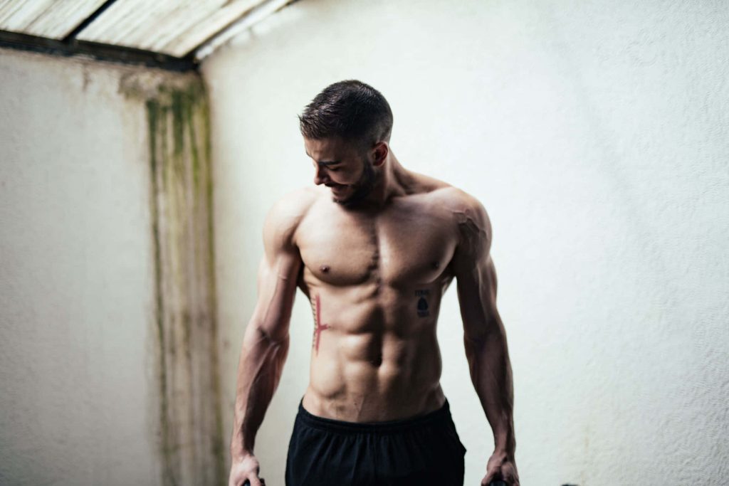 Muscular shirtless man with defined abs and biceps in minimalist soft light fitness wallpaper