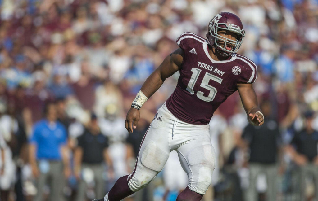 Myles Garrett in Texas A&M football uniform poised on field with blurred stadium crowd background Wallpaper