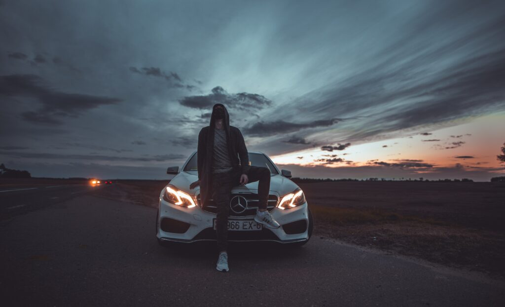 Mysterious Dusk Scene: Hooded Man by Mercedes under Dramatic Sky Wallpaper