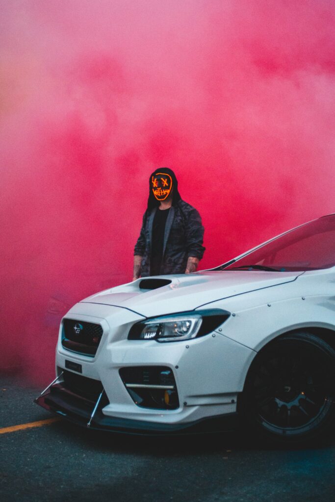 Mysterious Figure in Mask with White Car in Pink Smoke - Surreal Scene Wallpaper