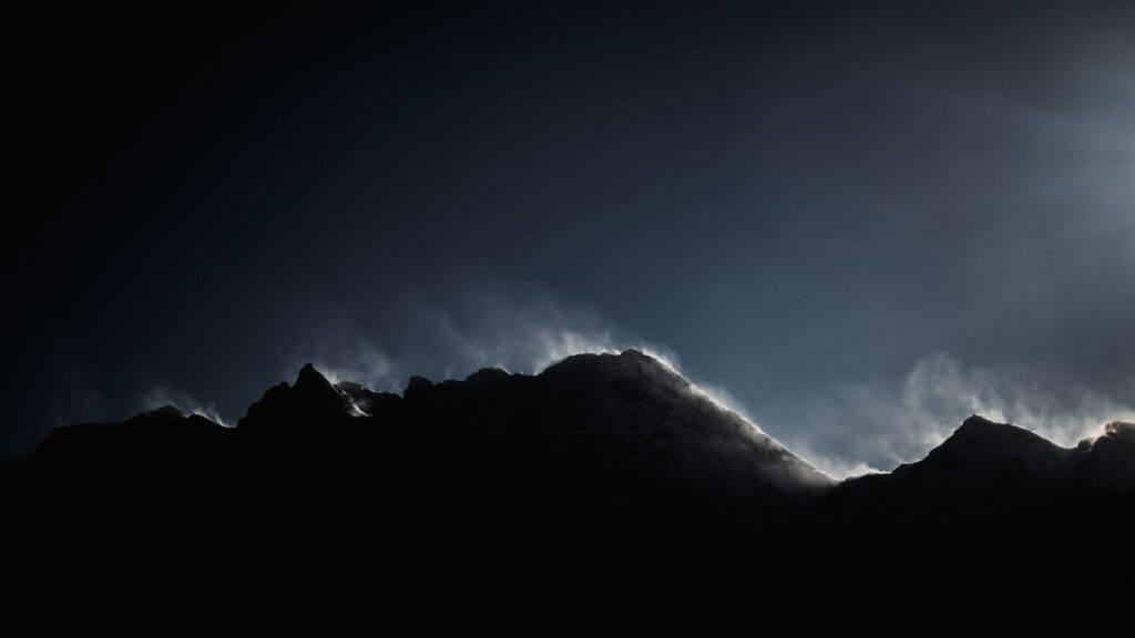Foggy mountain peak with dramatic shadows and soft highlights under a moody twilight sky Wallpaper