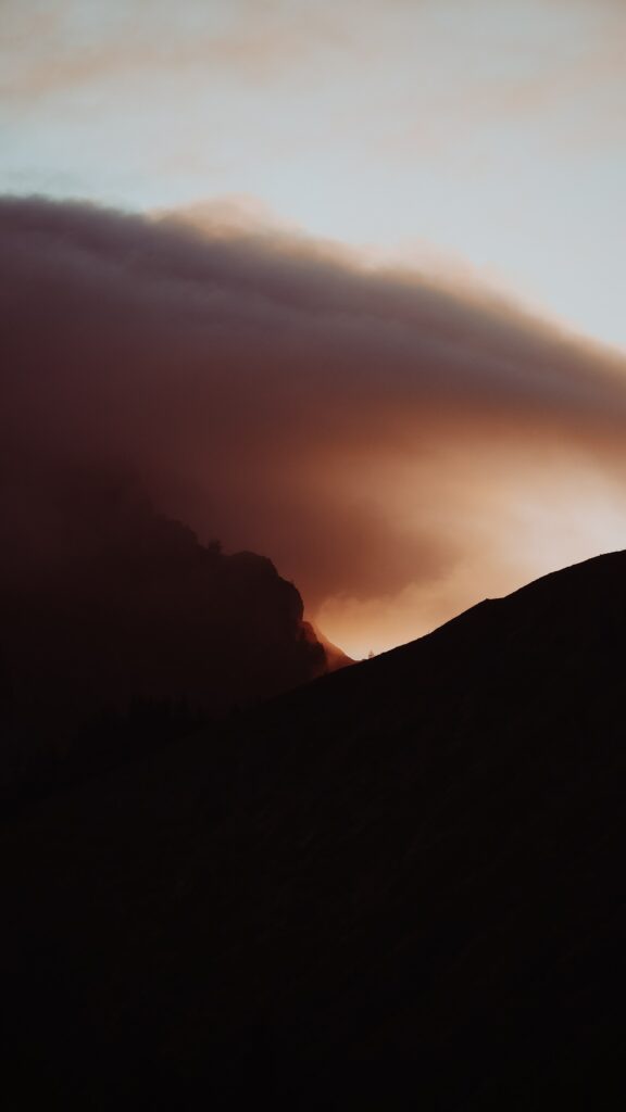 Silhouette of dark slope with rolling fog and smoky dusk light creating moody landscape wallpaper