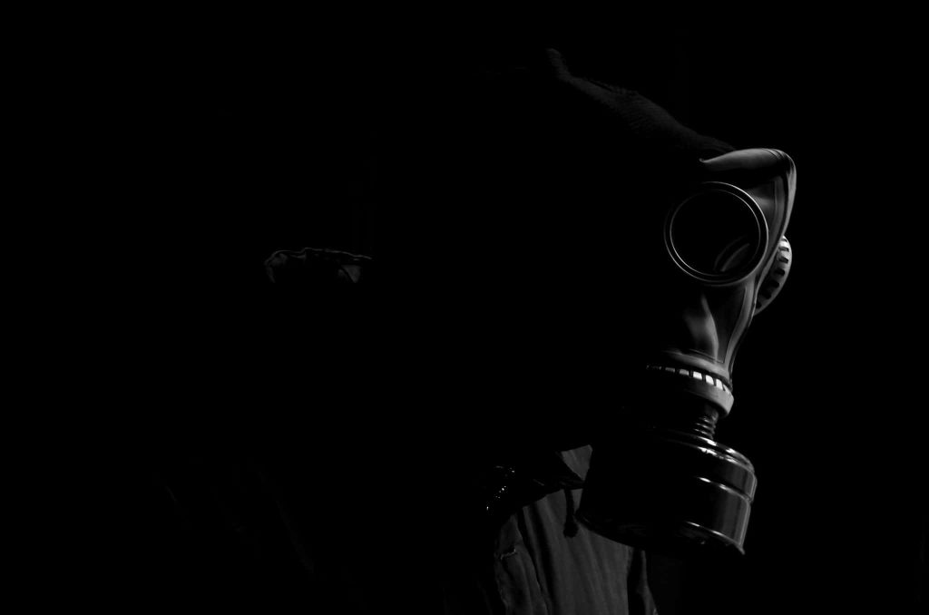 Moody black and white profile of a mysterious figure wearing a gas mask on dark background Wallpaper