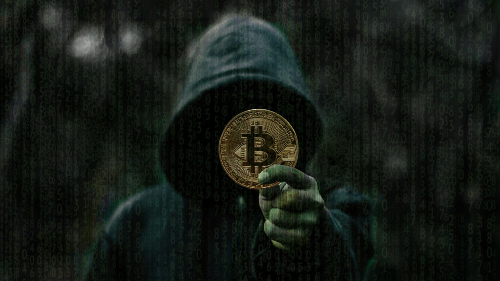 Hooded figure holding golden Bitcoin against dark digital code background symbolizing crypto anonymity Wallpaper