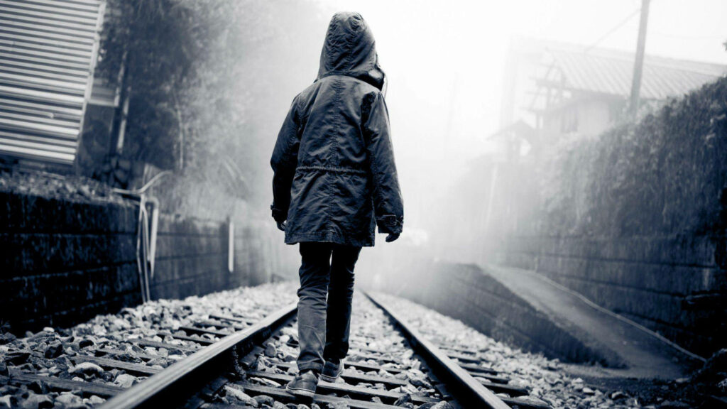 Lonely Journey: A Serene 1080p HD Background Depicting a Child Clad in a Hooded Jacket Strolling Along Desolate Train Tracks Wallpaper