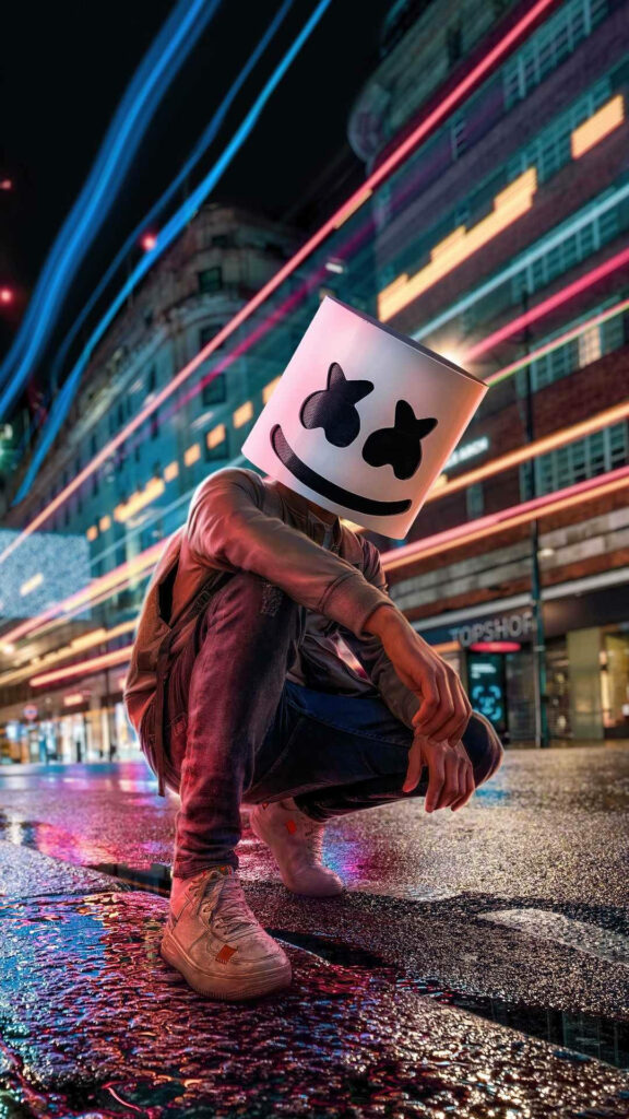 Marshmello's Enigmatic Presence: Stunning HD iPhone Wallpaper with the Iconic DJ Crouching Amid a Rainy Landscape, Adorned in His Signature Marshmallow Helmet and Dressed in a Stylish Black Jacket