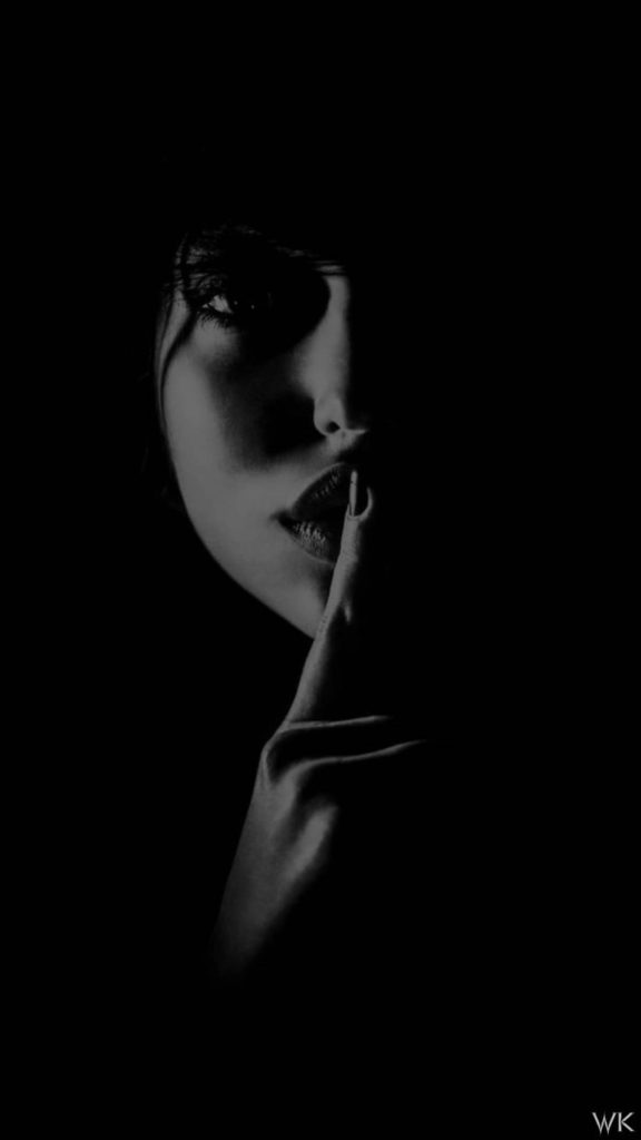 Monochrome portrait of woman making shhh gesture low-key lighting AMOLED wallpaper background