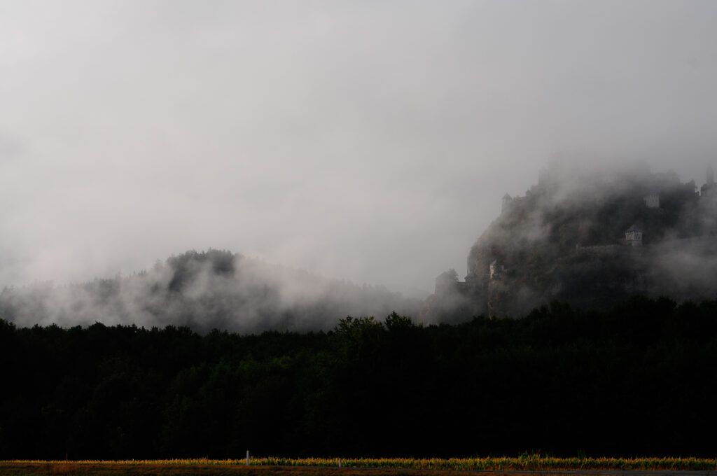 Mysterious mountain fortress rising through fog over dark dense forest moody landscape wallpaper