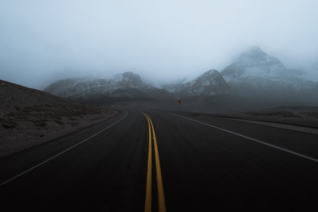 Winding mountain road with yellow lines fading into foggy rugged peaks in tranquil muted tones Wallpaper