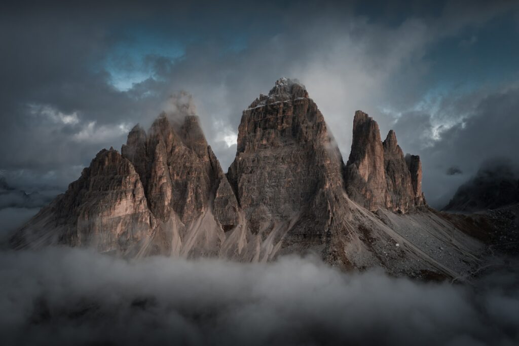 Dramatic mountain peaks and rugged rocks rising through swirling clouds with moody lighting Wallpaper