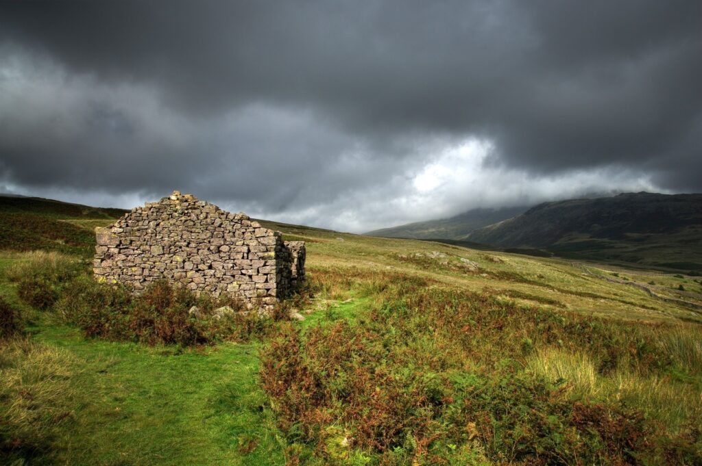 Stone ruins in rugged Scottish mountains under dramatic cloudy skies with wild grass and heather Wallpaper